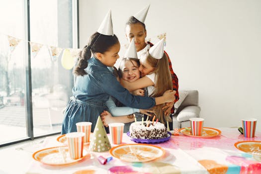 Children celebrating a birthday with joy, hugging and smiling around a festive table with cake and party hats.